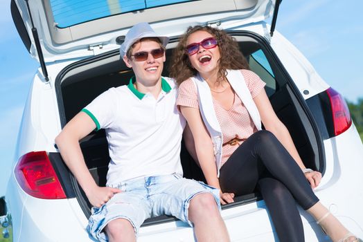 young couple sitting in the open trunk of a new car, a summer road trip