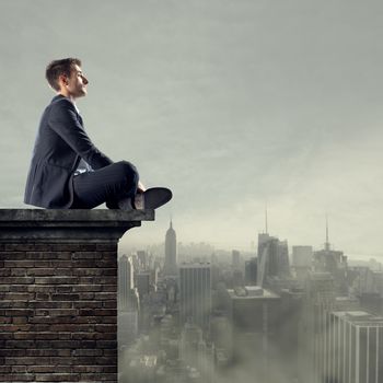 Businessman sitting on top of a building looking far away with cityscape on backgound.