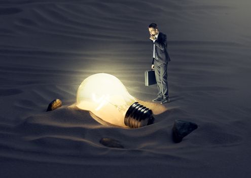 Businessman finding a light bulb in the dark.