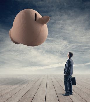 Businessman with briefcase contemplating a huge clay coin bank with sky on background.