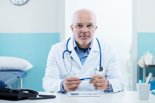 Senior doctor at his desk working with medical equipment in the background.