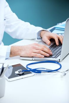 Doctor working at his desk with stethoscope, laptop and tablet.