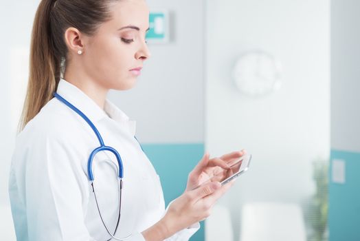 Portrait of a beautiful young female doctor in scrubs with stethoscope around neck using digital tablet.