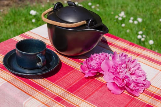 black ceramic teapot and cup with peony blossom on table outdoor