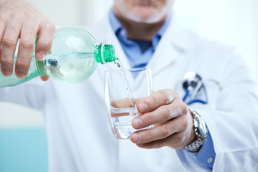 Doctor pouring water out of a bottle into a glass.