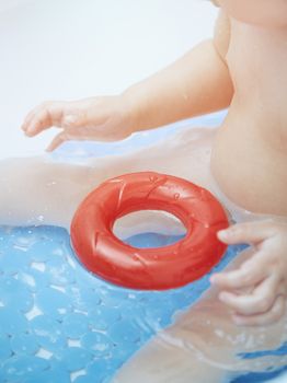 Ony year baby sitting in the bath and playing with toys