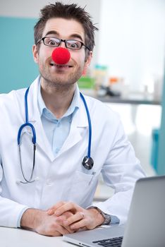 Funny young doctor with a clown's nose working at his desk