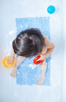 Ony year baby sitting in the bath and playing with toys