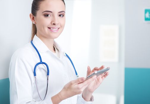 Portrait of a beautiful young female doctor in scrubs with stethoscope around neck using digital tablet.