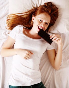 A young redhead woman eating Chocolate in Bed.