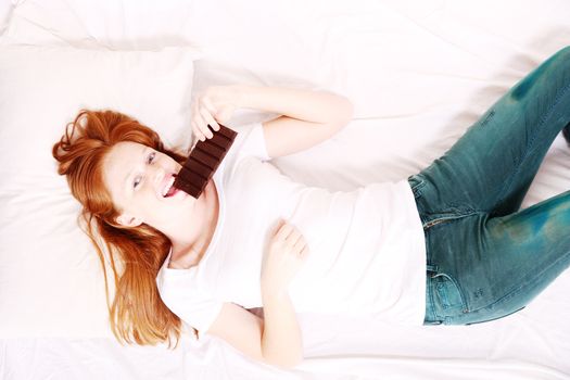 A young redhead woman eating Chocolate in Bed.