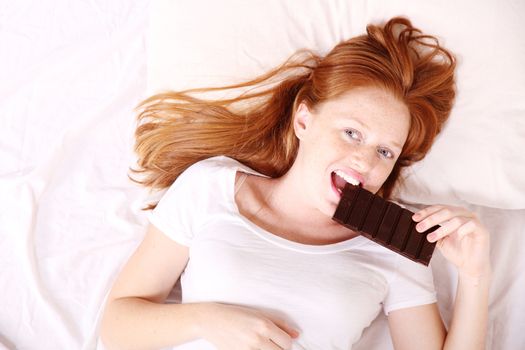 A young redhead woman eating Chocolate in Bed.