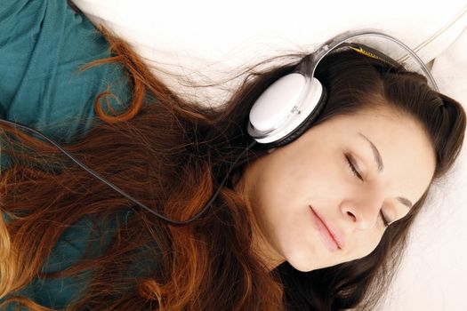 A young adult woman listening music with headphones in bed.