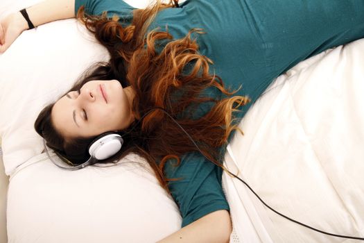 A young adult woman listening music with headphones in bed.