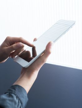 Woman using a digital tablet in front of a window, hands close-up.