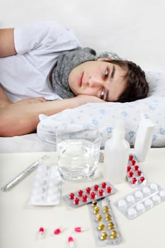 Sick Teenager lying on the Bed with a Pills on foreground