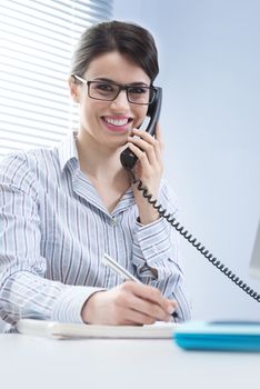 Beautiful woman with glasses answering phone calls at desk.