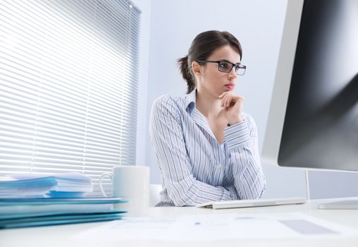 Pensive businesswoman staring at computer screen and touching her chin.