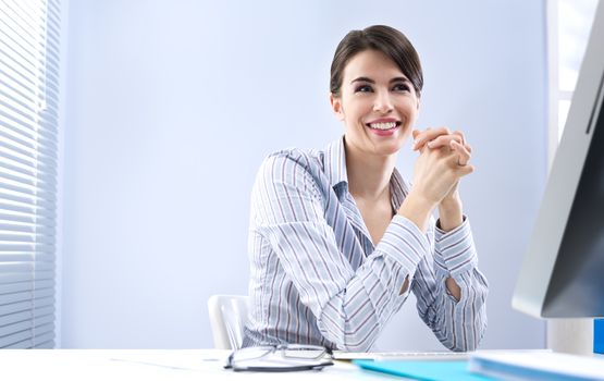 Beautiful businesswoman smiling at her desk with hands clasped.