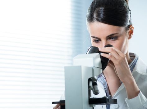 Young female researcher using microscope in the laboratory close up.