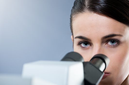 Attractive female researcher using microscope and looking at camera.