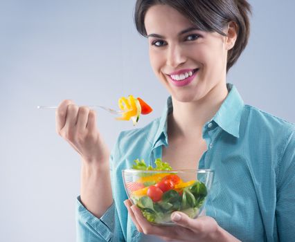 Young attractive woman eating salad and smiling at camera.