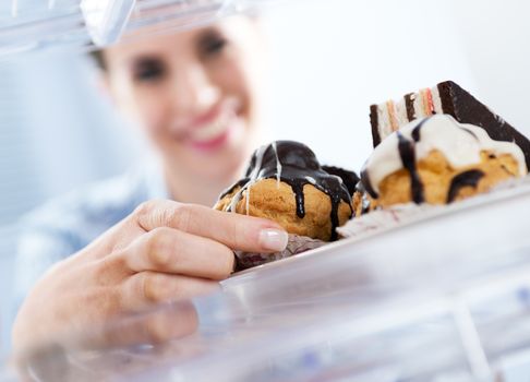 Young woman taking pastry with chocolate topping from fridge and smiling. 