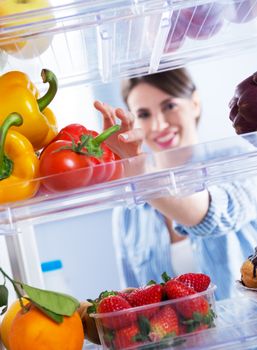 Young woman taking fresh healthy vegetables from refrigerator.