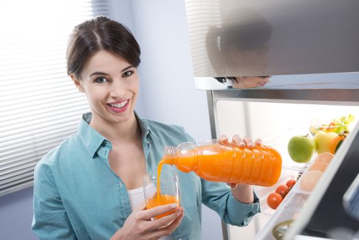 Cheerful young woman pouring fresh fruit juice into a glass.