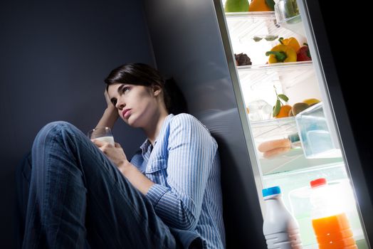 Sleepless sad woman sitting on kitchen floor having a glass of milk.