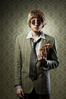 Funny guy holding a glass of whisky and posing against vintage wallpaper.