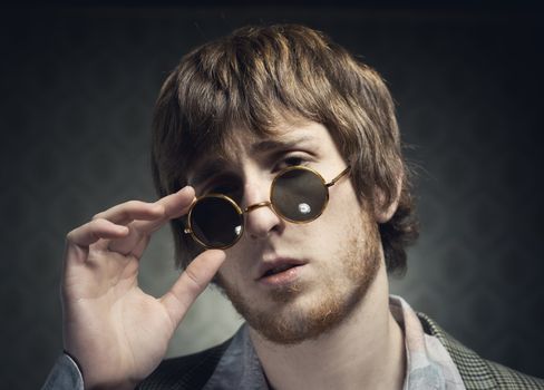 1960s style guy posing with circular glasses on vintage wallpaper background.