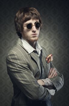 1960s style guy posing with circular glasses on vintage wallpaper background.