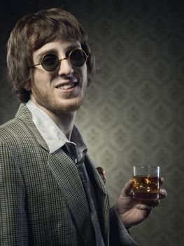 Funny guy holding a glass of whisky and posing against vintage wallpaper.