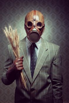 Man wearing a gas mask and holding ears of wheat.