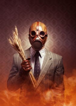 Man wearing a gas mask and holding ears of wheat with toxic smoke on background.