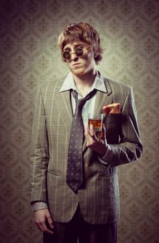 Funny guy holding a glass of whisky and posing against vintage wallpaper.