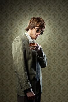 Funny guy holding a glass of whisky and posing against vintage wallpaper.