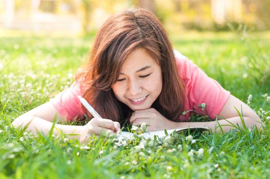 Happy Young Asian Woman Writing in Notebook and Smiling in Spring Garden.