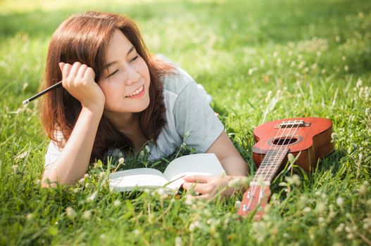 Female song writer. Thinking with notebook and little guitar on her side