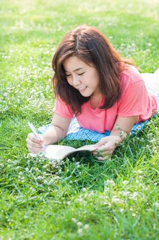 Happy Young Asian Woman Writing in Notebook and Smiling in Spring Garden.