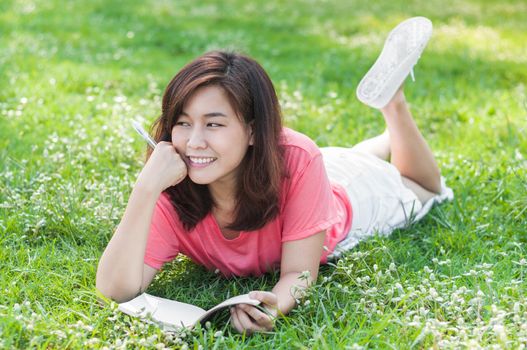 Happy Young Asian Woman Writing in Notebook and Smiling in Spring Garden.