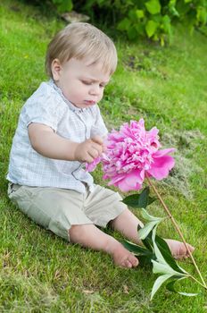 Baby boy with pink peony sitting on the grass