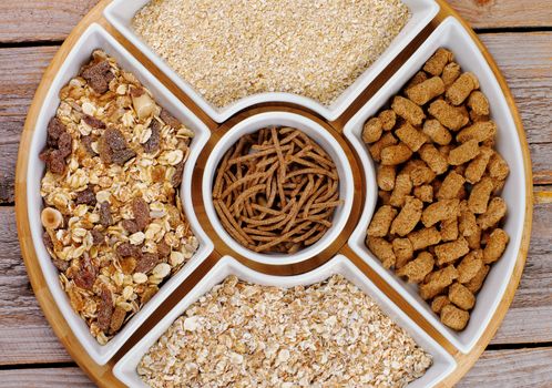 Various Muesli, Oat Flakes and Bran in White Plates closeup on Wooden background