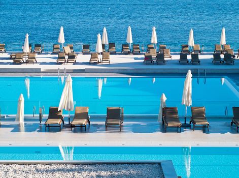 swimming pool with deckchairs and beach umbrellas, open sea in background