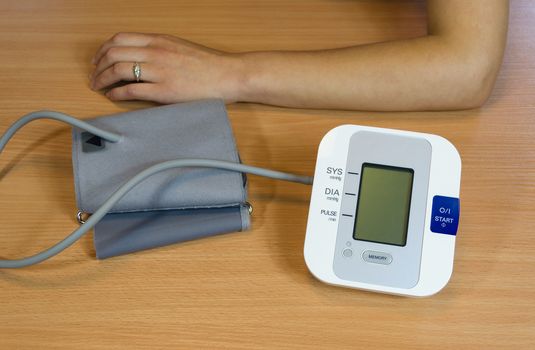 female hands and modern digital blood pressure measurement equipment on table