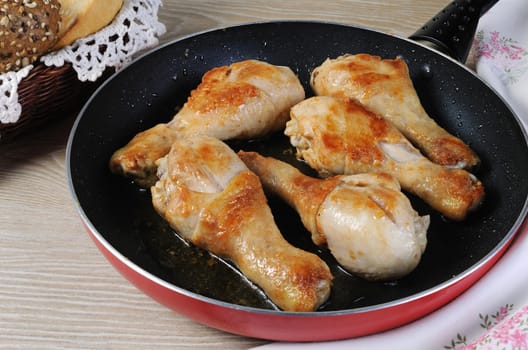 Ruddy fried chicken drumsticks in pan closeup