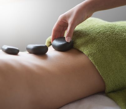 Young woman receiving a hot stone massage therapy at spa.