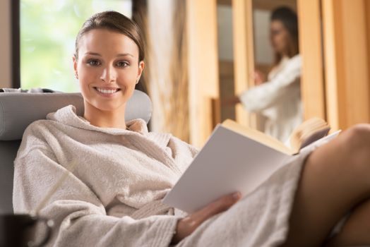 Young woman in bathrobe relaxing at spa and reading a book.