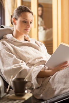 Young woman in bathrobe relaxing at spa and reading a book.